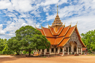 Thai temple surrounded by trees beneath a bright sky